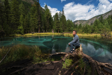 Man at Beautiful Geyser lake with thermal springs that periodically throw blue clay and silt from the ground. Altai mountains, Russia