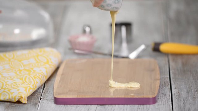 Woman pours melted white chocolate on the acetate sheet.