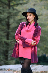 Glamour fashion model posing pretty outdoor in the autumn park wearing neon pink design sweater and hat.