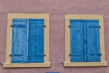 Two windows with  blue shutters on pink wall