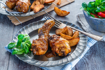 Chicken drumsticks in ginger beer sauce with potato wedges and salad on a plate