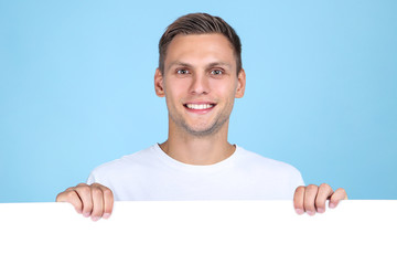 Young man with blank board on blue background