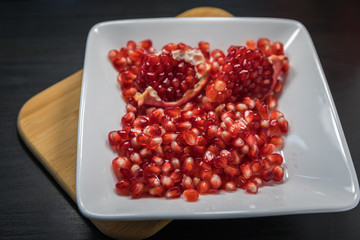 Delicious pomegranate seeds placed in glass jar with fresh organic pomegranates on rustic wooden background.Close up,Copy space
