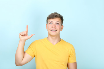 Young man with dental braces showing finger up on blue background