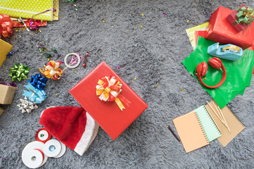 Christmas and Holiday Season Concept. Close up of christmas hat and big red gift box and decorate accessories, pencil, notebook and headphone on gray wool carpet in living room.