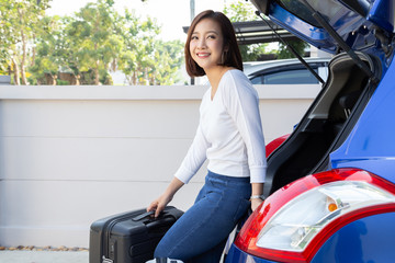 Young Asian woman packing suitcases into the trunk of her car for travel summer vacation