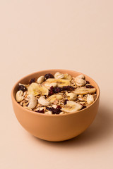 A fresh granola with dried and candied nuts and fruits in beige colour bowl closeup on beige bakground.