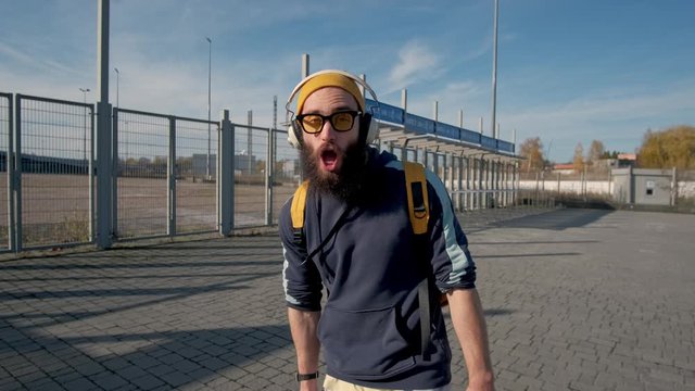 Portrait of a stylish bearded man in yellow clothes enjoying music with headphones on the blue sky background