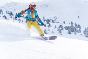 Young athlete girl in helmet and mask is riding on snowboard on snowy slope at winter day.
