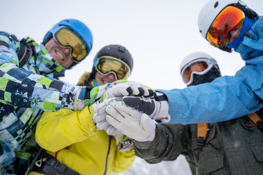 Photo from bottom of four happy snowboarders in helmet doing handshake .