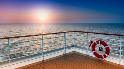 Beautiful scenic sunset view from the deck of a cruise ship with safety railing in the foreground.
