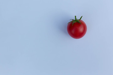 A red tomato lies on a grey paper sheet.