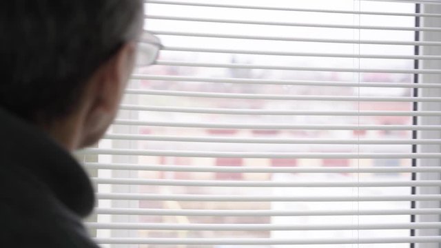 Watch the street through the blinds. Peep through the curtain. The old man's fingers opened the gap to look out at the street. An old man is trying to look through the curtain at the outside world. Se