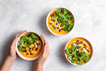 Three bowls of pumpkin soup with seeds and lettuce on light, white background 