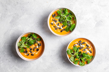 Three bowls of pumpkin soup with seeds and lettuce on light, white background 