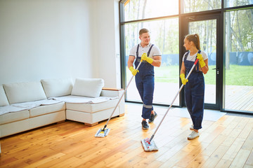 Mopping floor in uniform, yellow protective gloves, panoramic window background