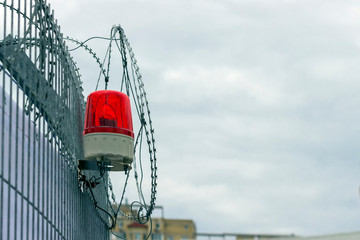 fence with barbed wire and a signal red lamp against a cloudy sky