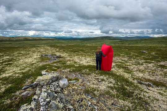 Young woman with red air lounger observing The desert landscape of Remdalen Valley in highlands of Norwegian Oppland