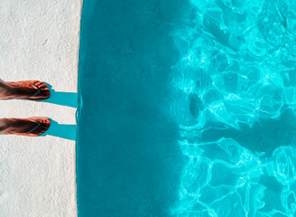 Top view of woman bare feet at a poolside. Tourist luxury blue swimming pool resort. Teal and orange style with copy space available.