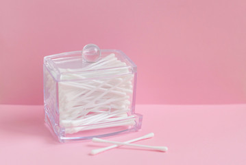 Cotton buds in glass box on pink background. Concept of hygiene and cleanliness.