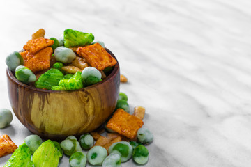 Japanese snacks with peas and wasabi lie in a brown wooden bowl and on a white marble surface