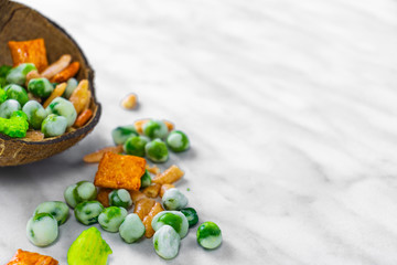 Japanese snacks with peas and wasabi lie in a coconut shell and on a white marble surface