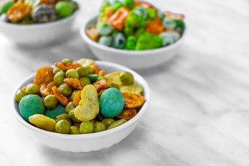 Japanese hot snacks with peanuts and wasabi lie in one of three white bowls on a white marble surface