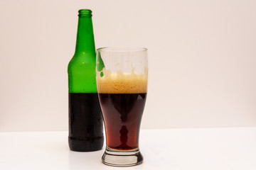 Half full transparent glass with dark beer and half empty green beer bottle on a light background