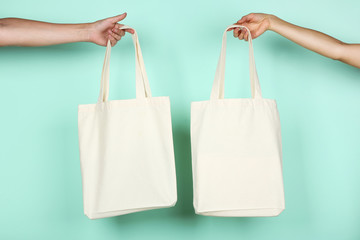 Female hands holding white cotton eco bags on mint background