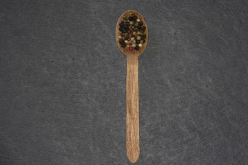Holzlöffel mit buntem Pfeffer auf einer dunkelen Schieferplatte