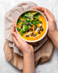 One bowl of pumpkin soup with seeds and lettuce on light, white background 