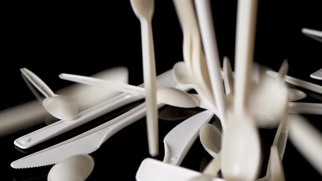 Pile of single-use plastic utensils fall from above on black surface.  Pollution and modern lifestyle concept.