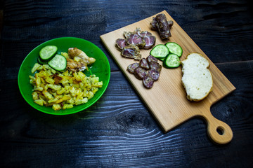 fried potatoes with vegetables, a bowl of potatoes and a wooden board with bacon and sausages