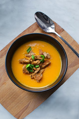 Delicious pumpkin soup in black plate with crackers