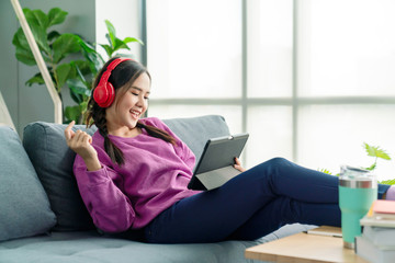 Candid of asian woman using tablet for watching online movie stream mobile device on sofa at living room. Young happy girl enjoying with entertainment media online on weekend. - Powered by Adobe