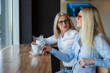 eautiful blonde with glasses and her elderly mother are sitting in a cafe and drinking coffee....