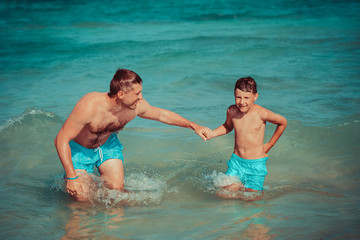 Fototapeta premium Dad and son are having fun during their summer holidays, they are swimming in the ocean, smiling and enjoying active leisure.