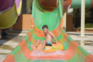Boy on floater sliding down slide in waterpark.
