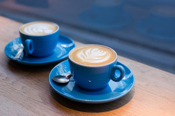 Two cups of cappuccino with latte art on wooden table, blue ceramic cup in cafe. Cafe culture.