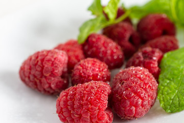 Close-up of wet raspberries and mint leaves, on a white plate in horizontal
