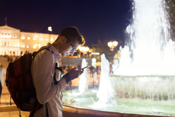 Man tourist using navigator on smartphone in Athens, Greece at night. Traveler going sightseeing