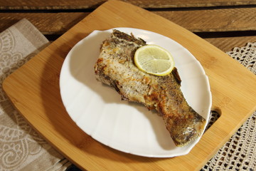 Baked stuffed fish luce tail with lemon  on white plate on wooden background