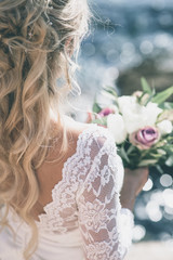 Beautiful bride in luxury wedding dress with bouquet at the sea side. Wedding by the sea. Bride walking around the sea near the place of the wedding ceremony. Back view