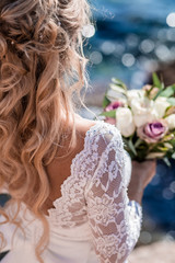 Beautiful bride in luxury wedding dress with bouquet at the sea side. Wedding by the sea. Bride walking around the sea near the place of the wedding ceremony. Back view