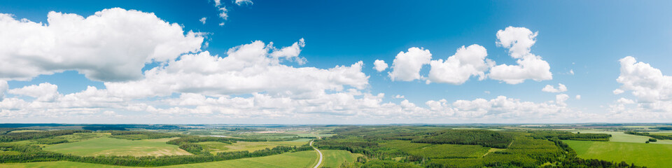 Fototapeta premium Aerial wide panorama of blue sky with white clouds and green countryside landscape in sunny summer day. Rural nature background