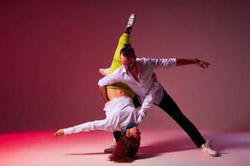 Sexy hip-hop woman in yellow pants and white pullover holding upside down for young dancer,...