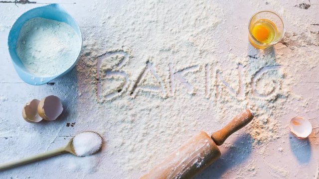 Das Wort backen wird in das Mehl geschrieben. Mehl auf K&uuml;chen abrbeitsplatte mit Backutensilien in der K&uuml;che.