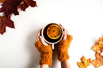 Autumn leaves on white background. Cup of tea keeped in hands in a gloves. Autumnal colors, minimalistic composition