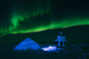 igloo and inukshuk illuminated under the northern lights
