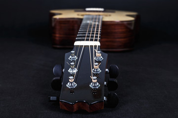 Tuning pegs on wooden machine head of six strings acoustic guitar neck on black background